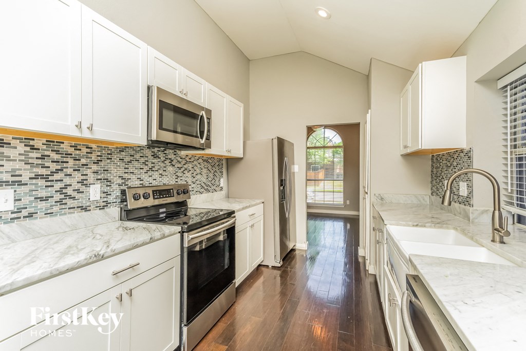 a kitchen with white cabinets and marble counter tops