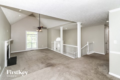 an empty living room with a ceiling fan and a staircase
