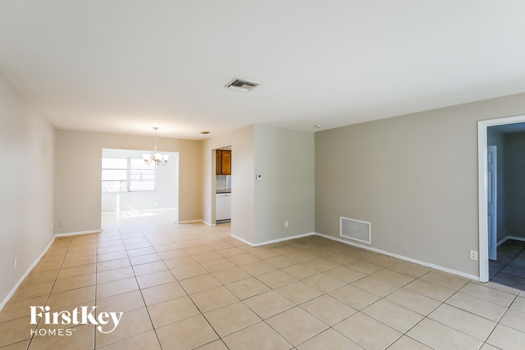an empty living room with tiled floors and a door to the kitchen