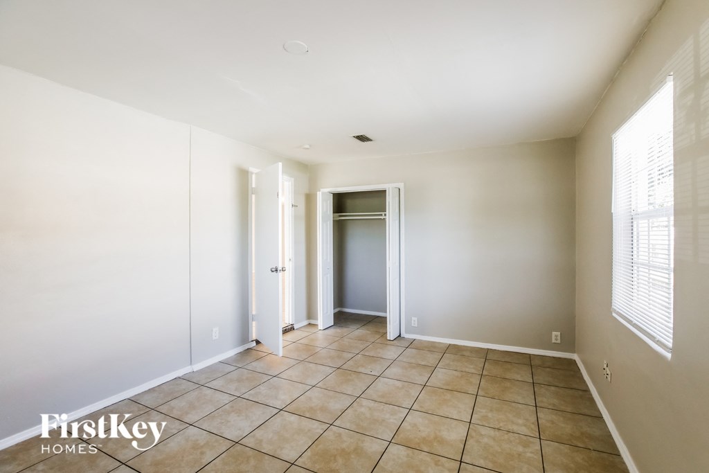 a hallway with white walls and tiled flooring and a closet
