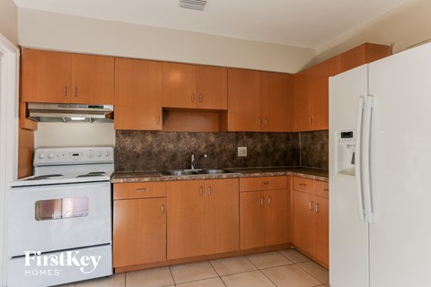 A kitchen with a white stove and a white refrigerator with wooden cabinets.