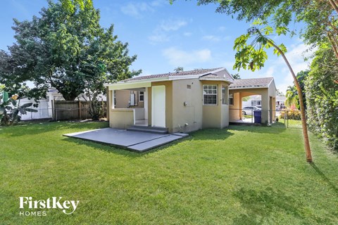 A house with a large lawn and trees in the background is for sale.