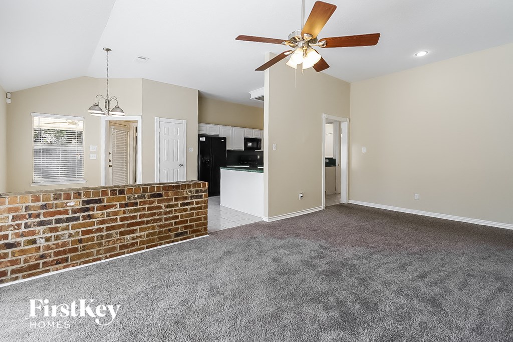 A spacious living room with a brick wall and a ceiling fan.