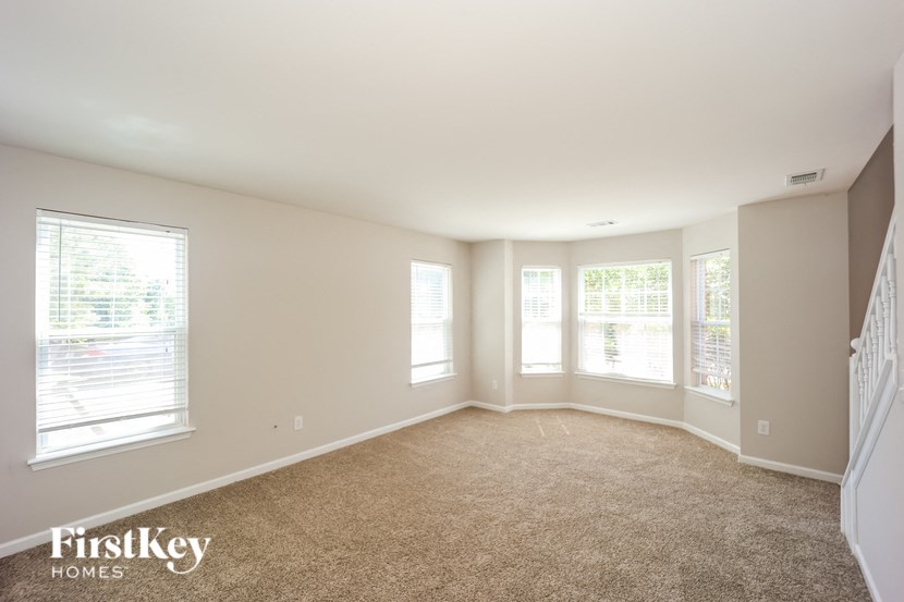 an empty living room with three windows and a staircase