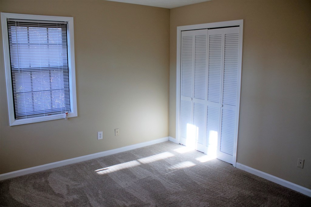 A room with a carpeted floor, a window with blinds, and a closed door.