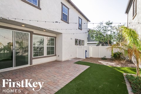 the backyard of a white house with a patio and grass