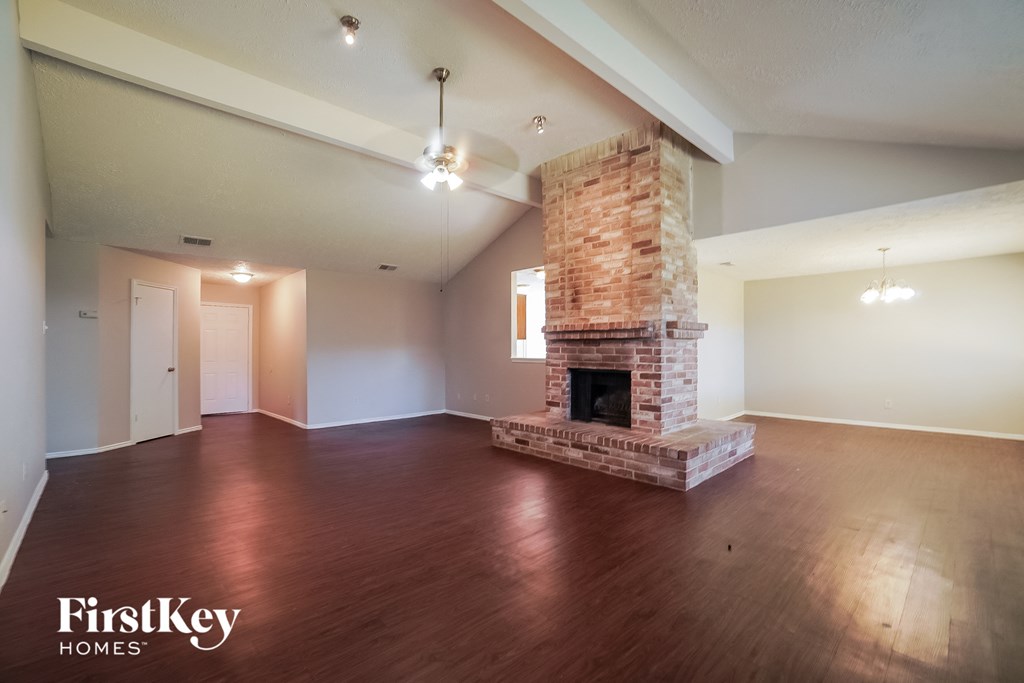 an empty living room with a brick fireplace and wooden floors