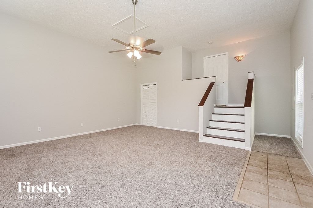 a spacious living room with stairs and a ceiling fan