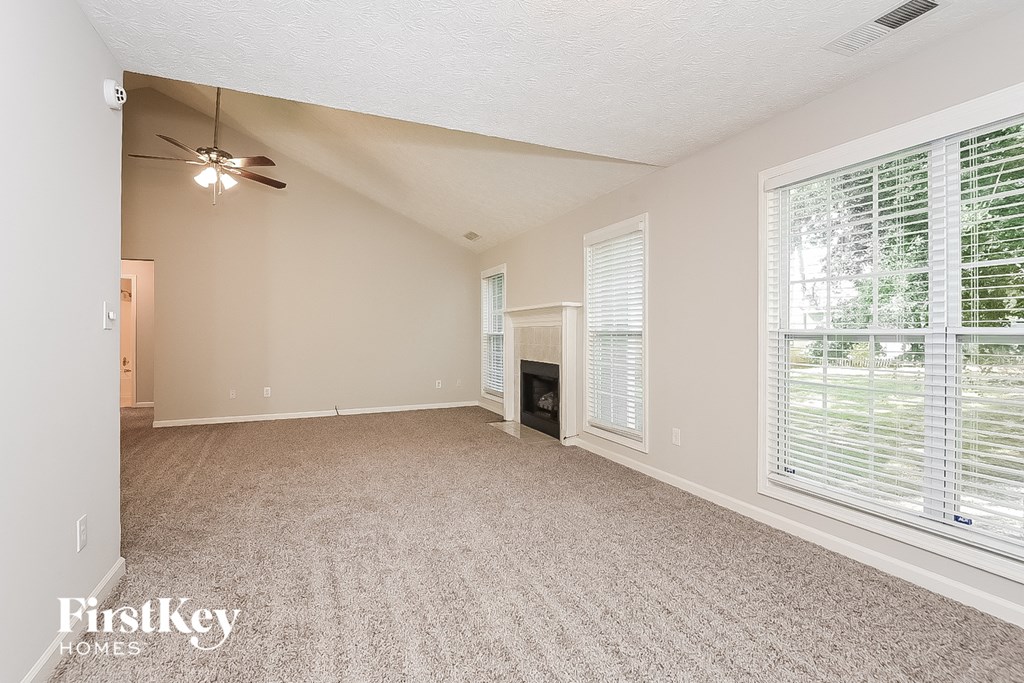 an empty living room with large windows and a ceiling fan