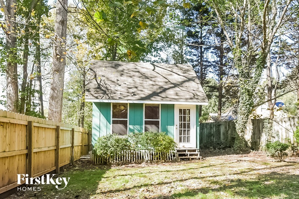 a small green house next to a fence and trees
