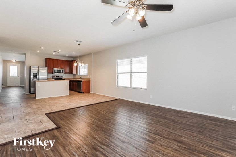 an empty living room with a kitchen and a ceiling fan