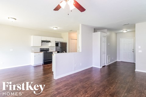 an empty living room and kitchen with wood flooring and a ceiling fan