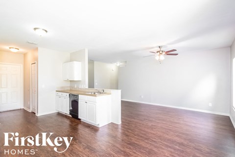 an empty living room with a kitchen and a ceiling fan