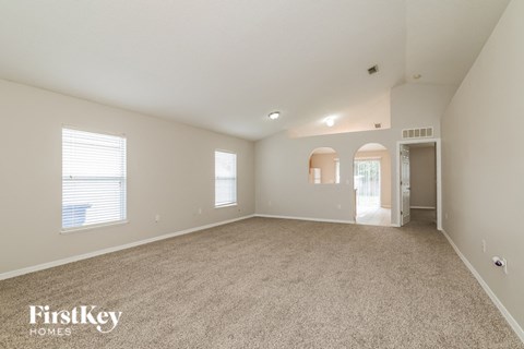 a spacious living room with carpet and a door to a hallway