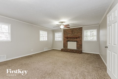 an empty living room with a brick fireplace and a ceiling fan