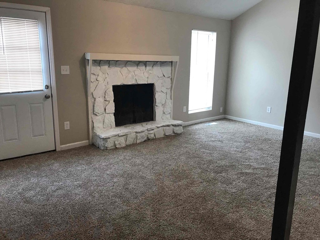 a carpeted living room with a stone fireplace and a door