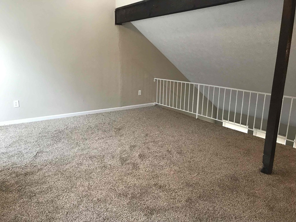 a room with a carpeted floor and a loft with a staircase