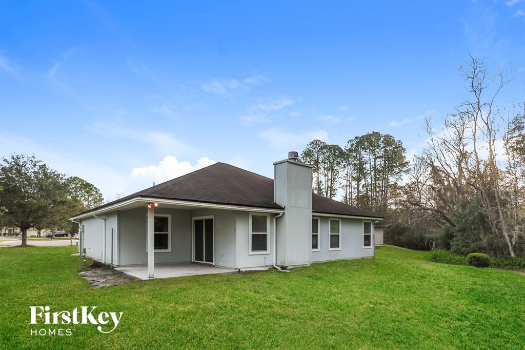 A white house with a chimney is surrounded by grass and trees.