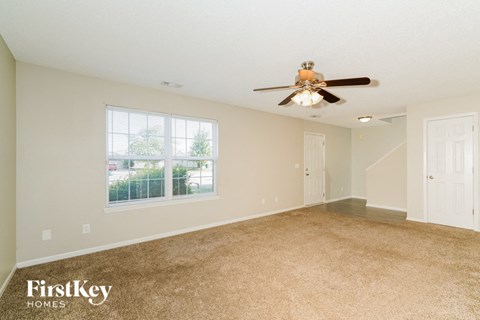 A spacious room with a carpeted floor and a ceiling fan.