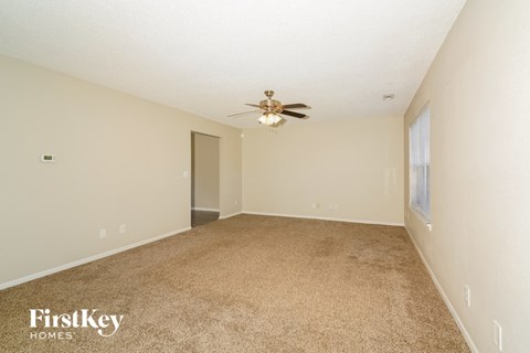 A carpeted room with a ceiling fan and a door.