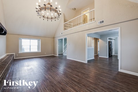 an empty living room with hardwood flooring and a chandelier