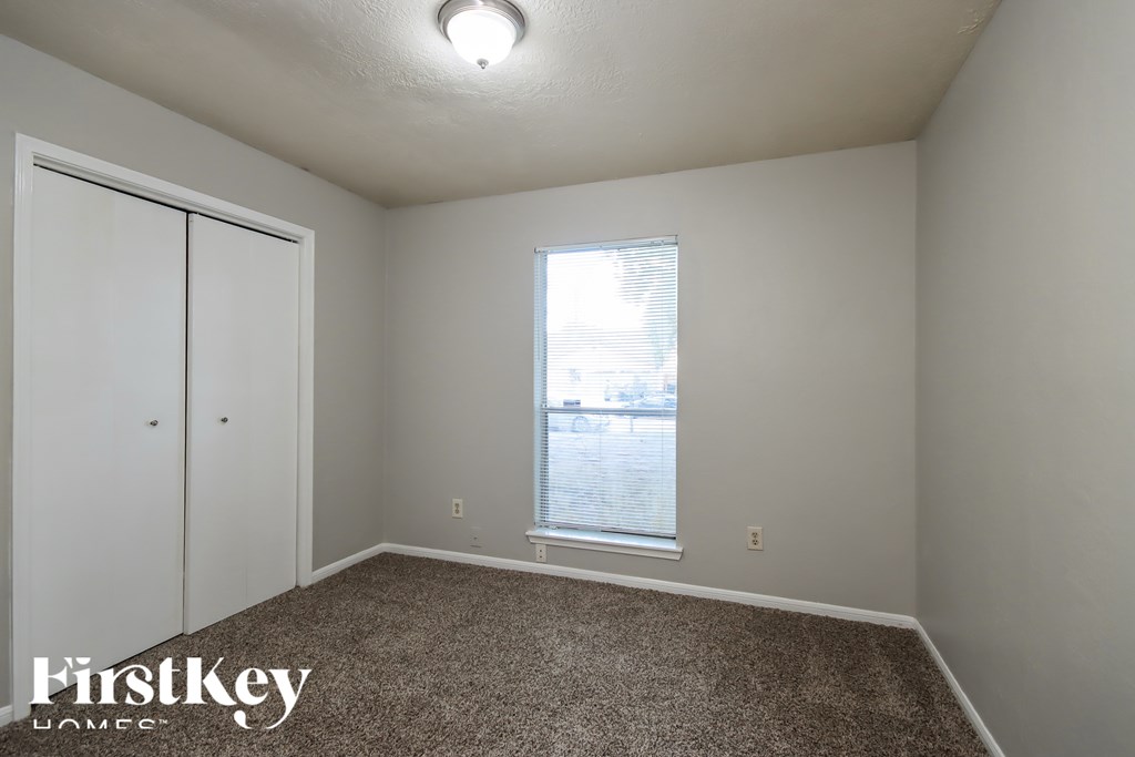 A room with a carpeted floor, a window, and a white door.