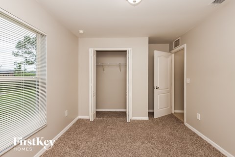 A bedroom with a carpeted floor and a window with blinds.