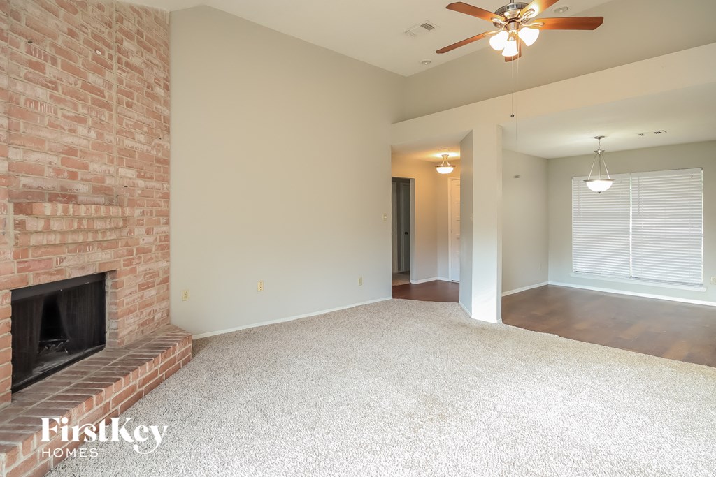 an empty living room with a brick fireplace and a ceiling fan
