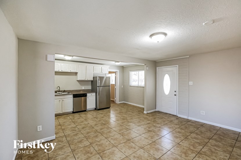 an empty living room with a kitchen with a stove and refrigerator
