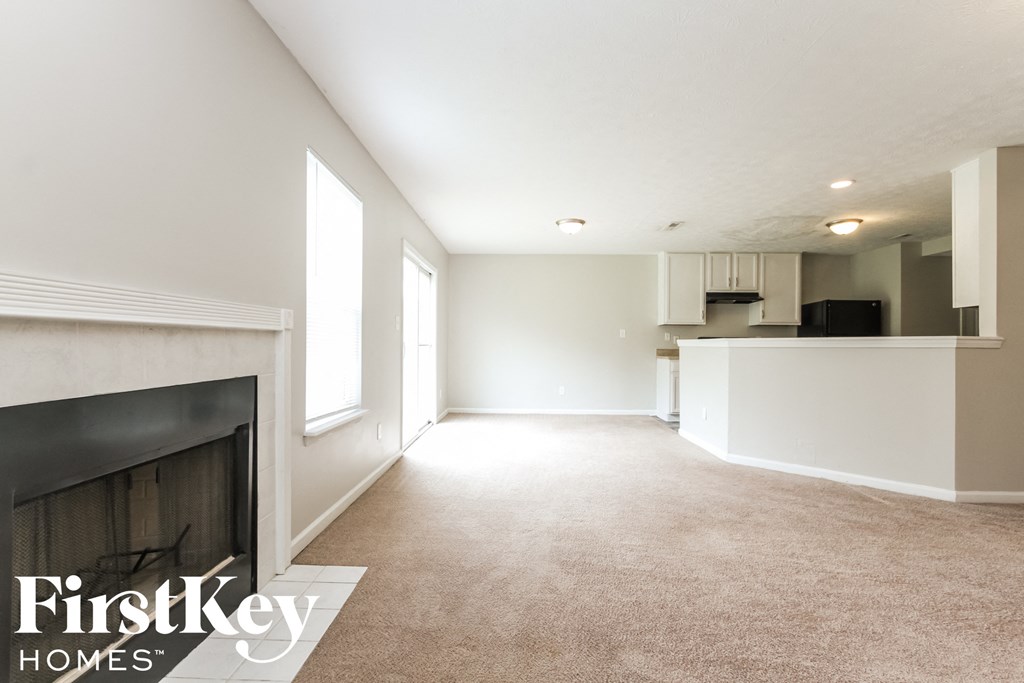 an empty living room with a fireplace and a kitchen
