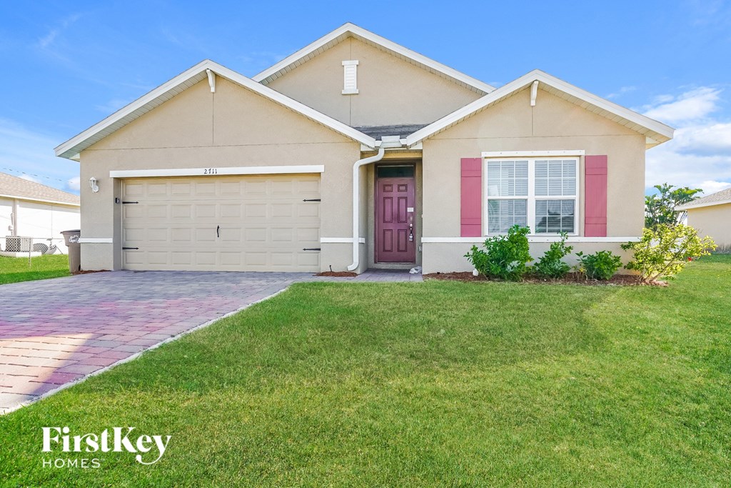 a beige house with pink shutters and a lawn