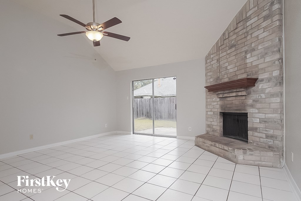 an empty living room with a stone fireplace and a ceiling fan