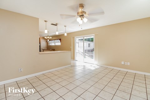 an empty living room with a ceiling fan and a door to the kitchen
