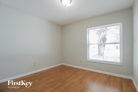 a bedroom with white walls and wood floors and a window