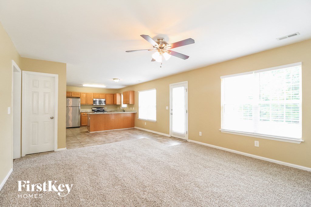 A spacious living room with a carpeted floor and a ceiling fan.