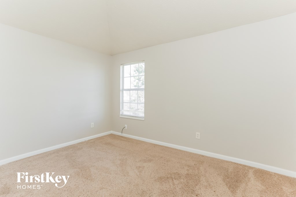 a bedroom with white walls and carpet and a window