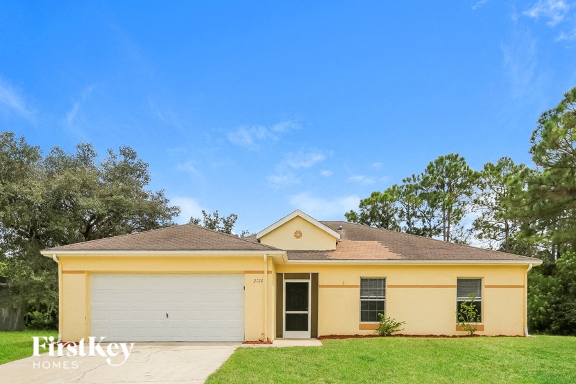 A yellow house with a garage door and a tree in the background.