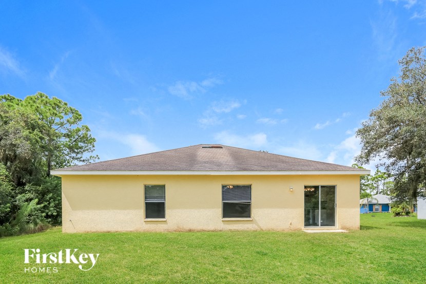 A small house with a brown roof is surrounded by green grass and trees.