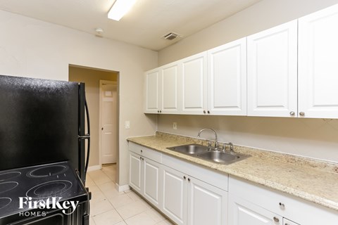 A kitchen with white cabinets and a black fridge.