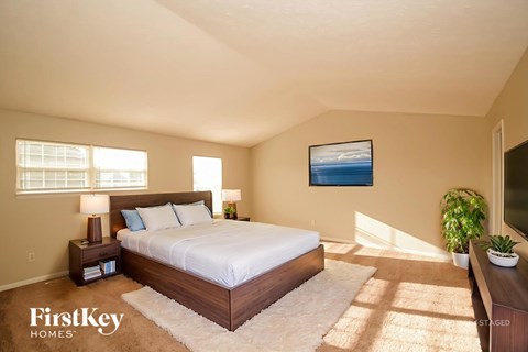 A bedroom with a large bed, a painting on the wall, and a potted plant.