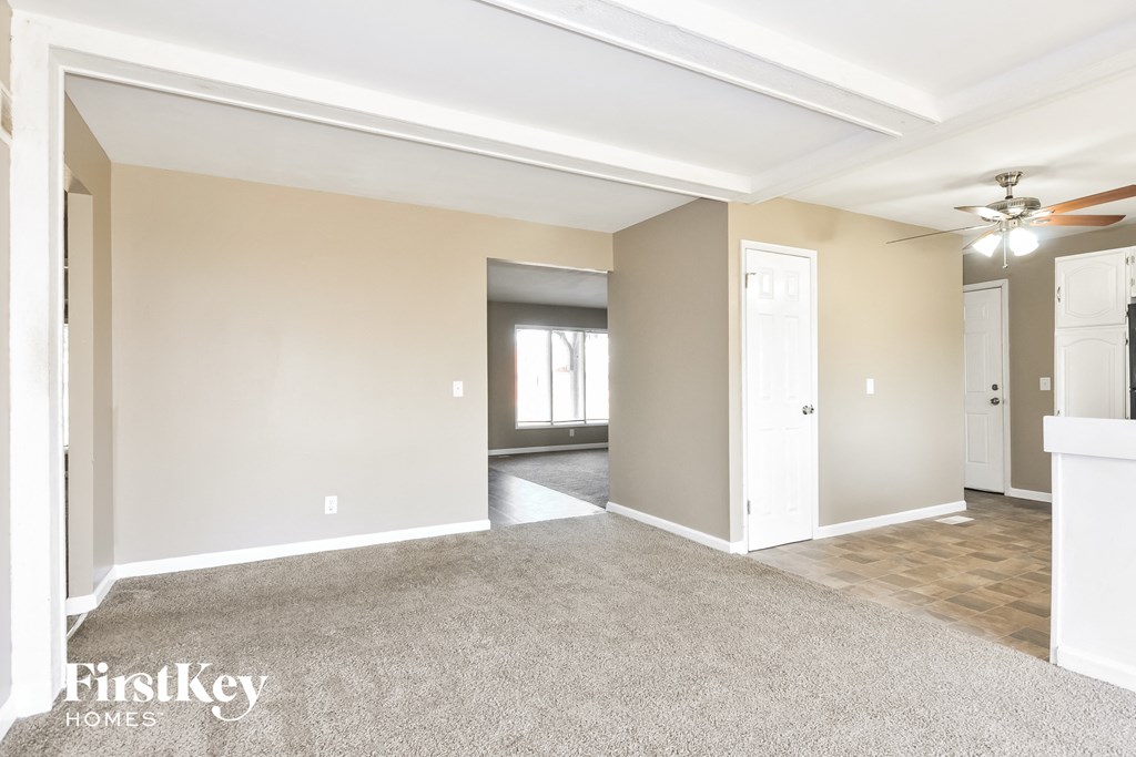 A spacious room with a carpeted floor and a white ceiling fan.
