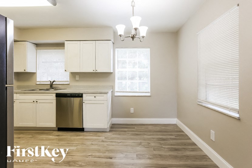 A kitchen with a stainless steel trash can and wooden floors.