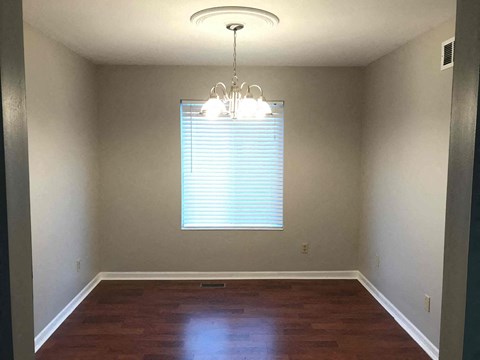 an empty dining room with a window and a chandelier