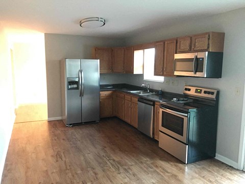 an empty kitchen with stainless steel appliances and wooden floors