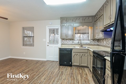 A kitchen with wooden floors and a black fridge.
