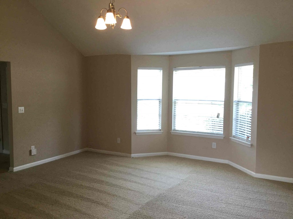 an empty living room with three windows and a carpeted floor