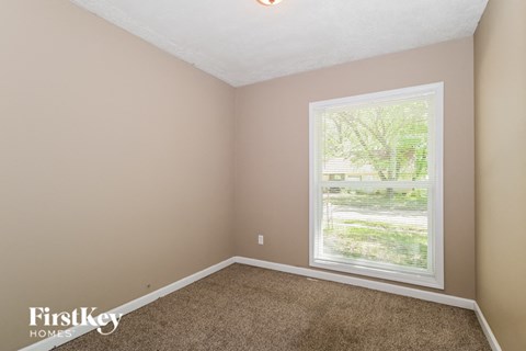 A room with a carpeted floor and a window showing a view of trees and a building outside.