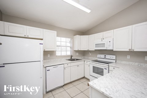 A kitchen with white cabinets and appliances, with a FirstKey Homes logo on the bottom left.