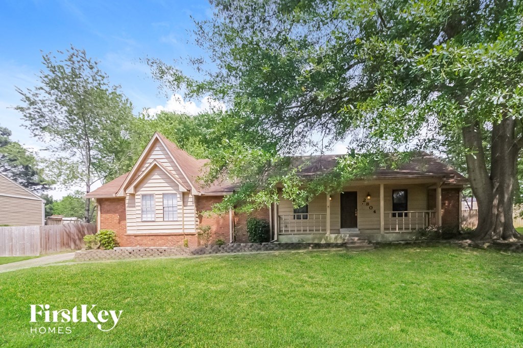 a small brown house with a yard and a large tree