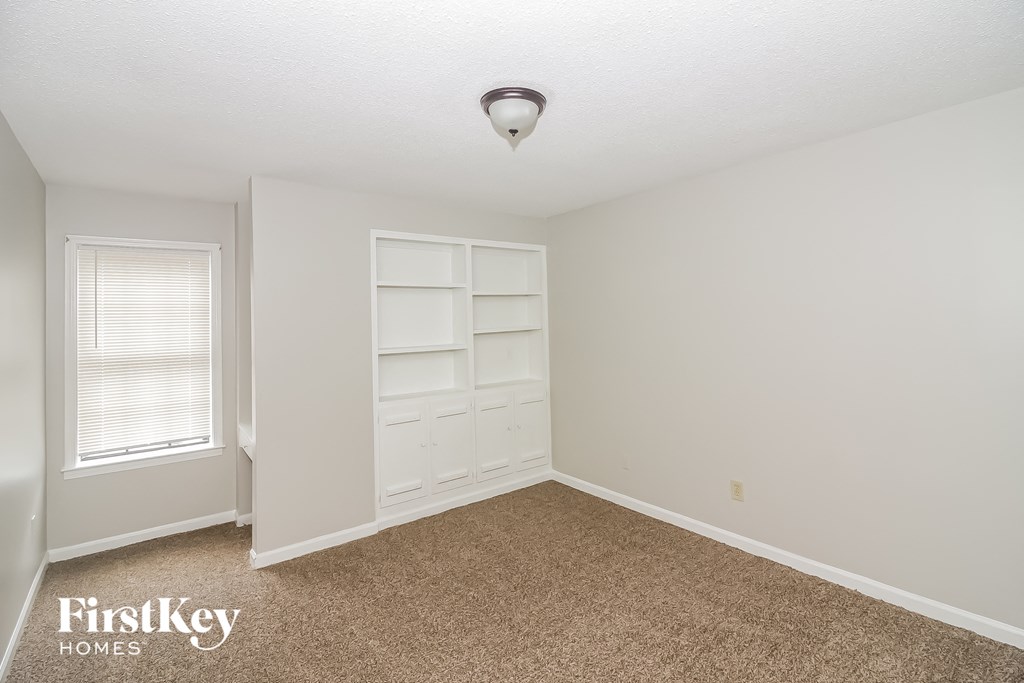 a bedroom with white shelves and a window and a carpeted floor